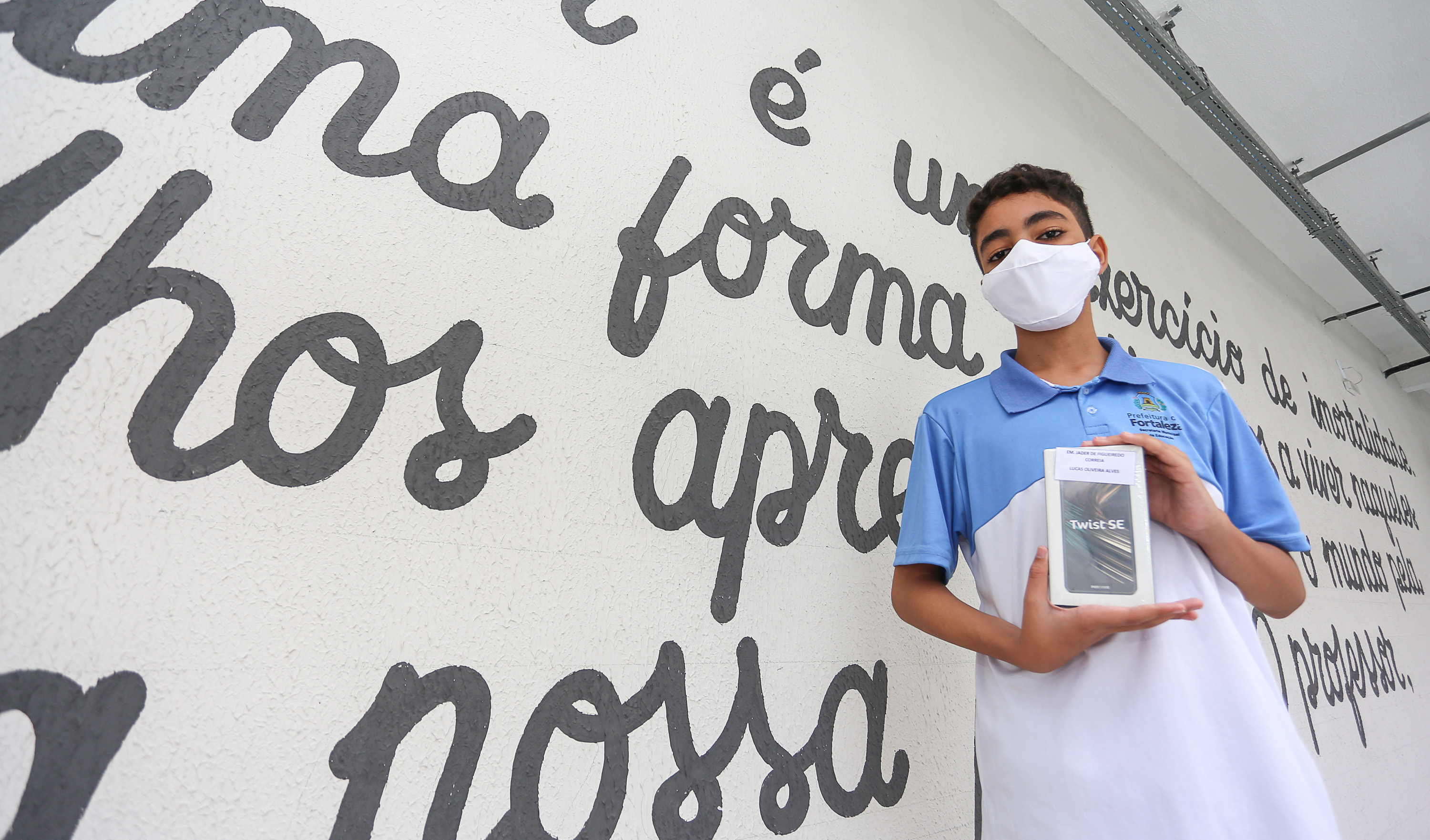 garoto de óculos, máscara e vestindo farda das escolas municipais, segurando caixa de smartphone e posando para a foto